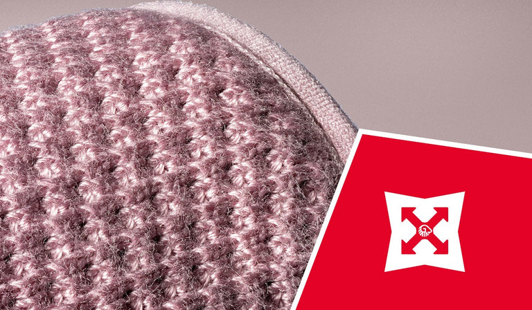 Rosa-braun gestrickter Stoff mit Zopfmuster neben rotem Schild mit weißem Pfeil-Logo auf neutralem Hintergrund