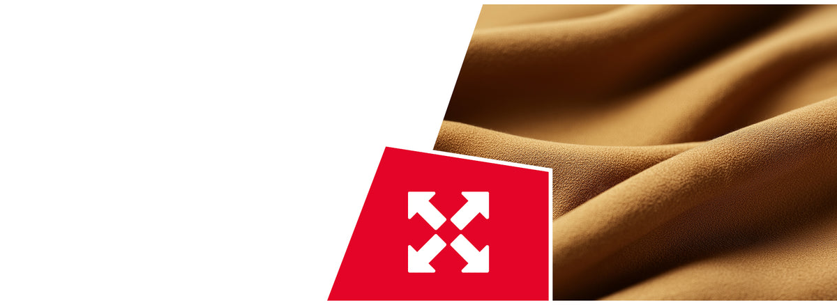 Nahaufnahme eines cognacbraunen, elastisch wirkenden Stoffes mit feiner Struktur, der in sanften Wellen liegt. In der unteren linken Ecke befindet sich ein rotes Quadrat mit einem weißen Symbol aus vier auseinander zeigenden Pfeilen – ein Hinweis auf Dehnbarkeit oder Flexibilität des Materials.
