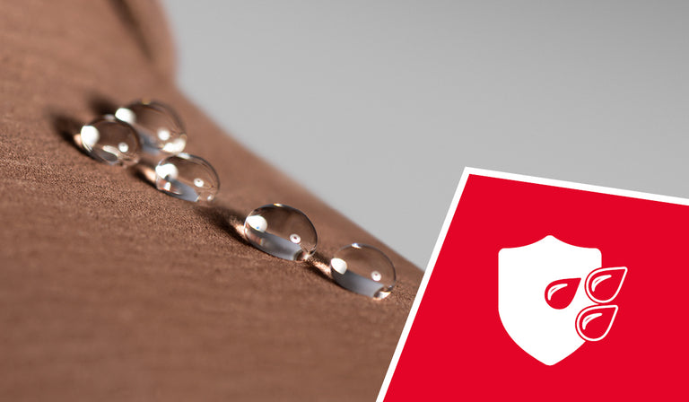 Mehrere Wassertropfen perlen auf der Oberfläche eines braunen, texturierten Materials ab – ein Hinweis auf wasserabweisende Eigenschaften. In der rechten unteren Ecke ist ein rotes Quadrat mit einem weißen Symbol zu sehen: ein Schutzschild mit drei Wassertropfen, das für wasserabweisenden Schutz steht.