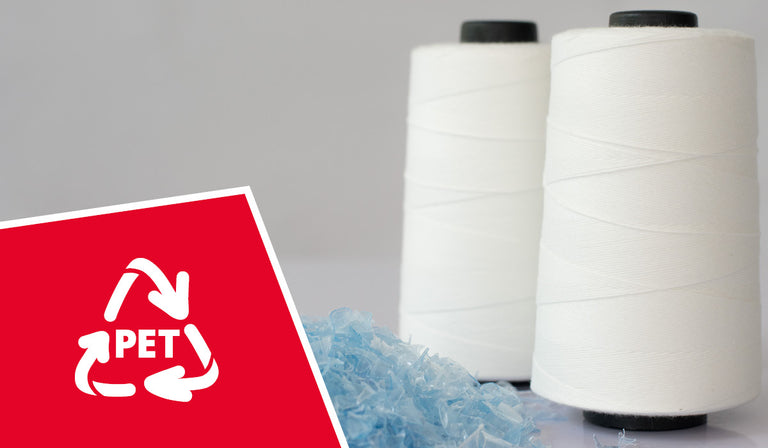Zwei große weiße Garnspulen stehen nebeneinander auf hellem Untergrund. Davor liegt ein kleiner Haufen bläulicher, recycelter PET-Kunststoffschnipsel. In der unteren linken Bildecke ist ein rotes Feld mit dem weißen Recycling-Symbol und der Aufschrift „PET“ zu sehen – ein Hinweis auf die Wiederverwertung von Kunststoff zu Garn.