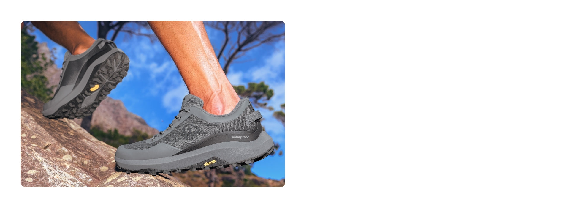 Nahaufnahme eines grauen Wanderschuhs (Wool Trail X von Giesswein) mit tiefem Profil auf einem steinigen Hang. Die Schuhe haben eine Vibram-Sohle und sind als „waterproof“ gekennzeichnet. Ein Bein ist beim Auftritt zu sehen, im Hintergrund zeigen sich blauer Himmel, Felsen und Bäume.