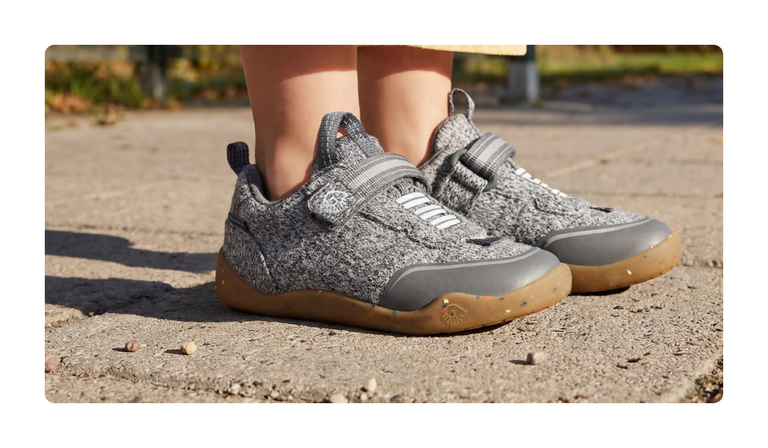 Nahaufnahme grauer Giesswein Kinder-Sneaker mit Merino-Obermaterial, Klettverschluss und honigfarbener Sohle auf einem Weg.
