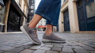 Person in Jeans und grauen Sneakers geht durch eine Altstadtgasse mit Kopfsteinpflaster