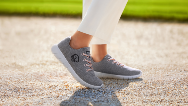 Seitenansicht von Person in weißer Hose mit grauen Giesswein Merino-Sneakern auf Kiesweg im Freien