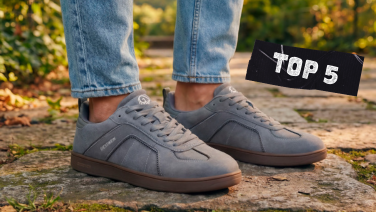 Nahaufnahme von Füßen in hellgrauen Wildleder-Sneakern auf Kopfsteinpflaster, mit einem schwarzen Aufkleber mit der Aufschrift „TOP 5" im oberen rechten Bildbereich.