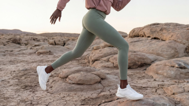 Frau im Laufschritt über felsigen Untergrund, sichtbar von der Taille abwärts. Sie trägt mintgrüne Leggings, einen altrosa Ärmel ist oben im Bild zu erkennen, an den Füßen weiße Giesswein Sneaker.