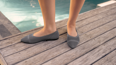  Nahaufnahme zweier Füße in grauen Strick-Ballerinas auf einem Holzsteg am Pool.