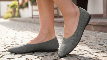Nahaufnahme von Füßen in grauen Giesswein Strick-Ballerinas, stehend auf einem Kopfsteinpflaster.