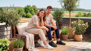 Zwei Personen sitzen auf einer Holzbank auf einer Terrasse mit Lavendel und Topfpflanzen, tragen weiße und schwarze Giesswein Merino Runner Sneaker.