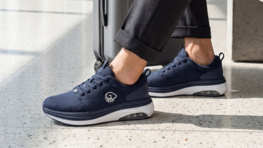 Nahaufnahme der Füße einer Person auf einem Terrazzoboden. Sie trägt dunkelblaue Merino Wolle Sneaker mit weißer Sohle und sichtbarem Air-Cushion-Element in der Ferse. Das Giesswein-Logo ist seitlich am Schuh zu erkennen.