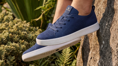Nahaufnahme eines dunkelblauen Giesswein Merino-Sneakers mit weißer Flachsohle vor mediterraner Bepflanzung und Steinen.