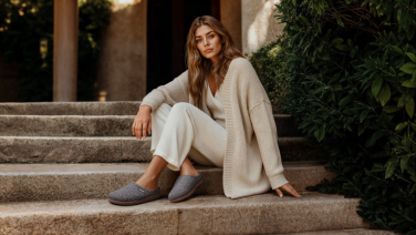Frau in beigefarbenem Loungewear-Outfit sitzt entspannt auf einer Steintreppe und trägt dunkelgraue Giesswein Wollschuhe
