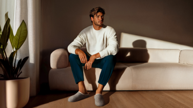 Mann in beigen Hausschuhen sitzt entspannt auf beigem Sofa