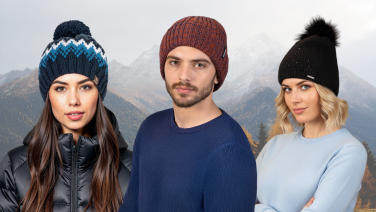 Drei junge Menschen in bunten Strickmützen vor verschneiter Berglandschaft