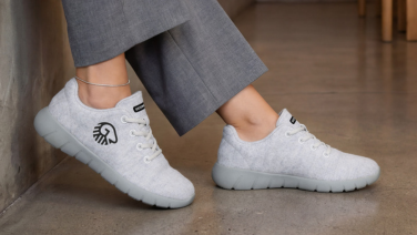 Nahaufnahme von weiblichen Beinen in grauer Hose und cremeweißen Merino-Sneaker von Giesswein auf Betonboden.