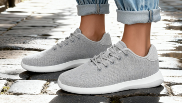 Nahaufnahme hellgrauer Giesswein Merino-Sneaker mit weißer Sohle auf Kopfsteinpflaster, getragen zu aufgekrempelten Jeans.