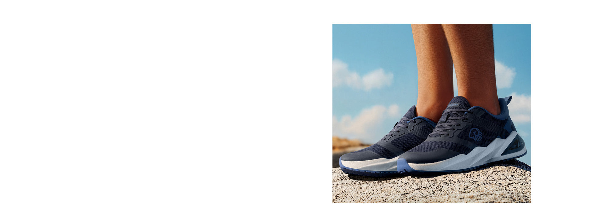 Nahaufnahme eines Paars dunkelblauer Sportschuhe (Wool Peak von Giesswein) auf einem hellen Felsen bei Tageslicht. Die Schuhe haben eine weiße, dicke Zwischensohle und ein sportliches Mesh-Design. Im Hintergrund ein klarer Himmel mit wenigen Wolken und sandfarbene Felsen in der Ferne.