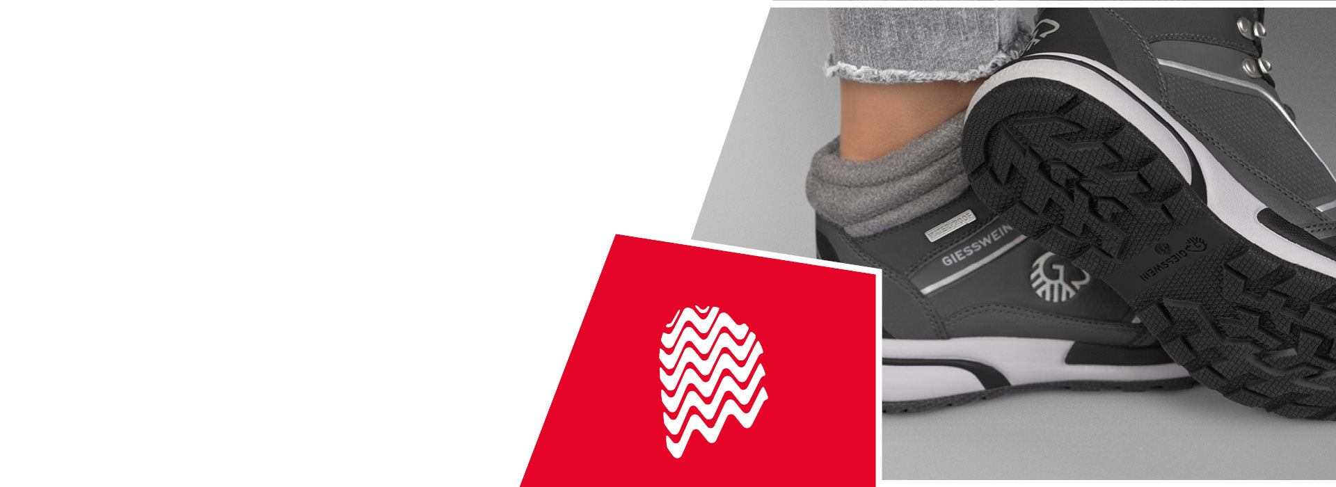 Nahaufnahme eines grauen Wanderschuhs (Wool Cross X Alpine von Giesswein) mit dicker, stark profilierter Gummisohle und sichtbarem GIESSWEIN-Logo an der Seite und auf der Sohle. Der Schuh wird von einer Person mit hochgekrempelter grauer Jeans und grauen Wollsocken getragen. Im Bild befindet sich ein rotes Quadrat mit einem stilisierten, weißen Fingerabdruck aus gewellten Linien – Symbol für Profil oder Griffigkeit.