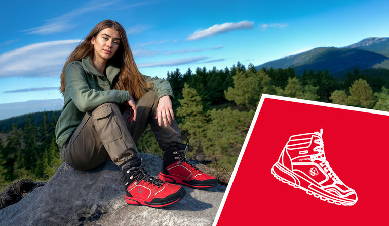Eine junge Frau sitzt entspannt auf einem großen Felsen inmitten einer waldreichen Berglandschaft. Sie trägt eine grüne Fleecejacke, olivfarbene Cargohose und auffällige rote Wanderschuhe (Wool Cross X Alpine von Giesswein) mit schwarzem Schaft und reflektierenden Details. Im unteren Bildbereich ist ein rotes Feld mit einer weißen, stilisierten Zeichnung eines Wanderschuhs zu sehen.