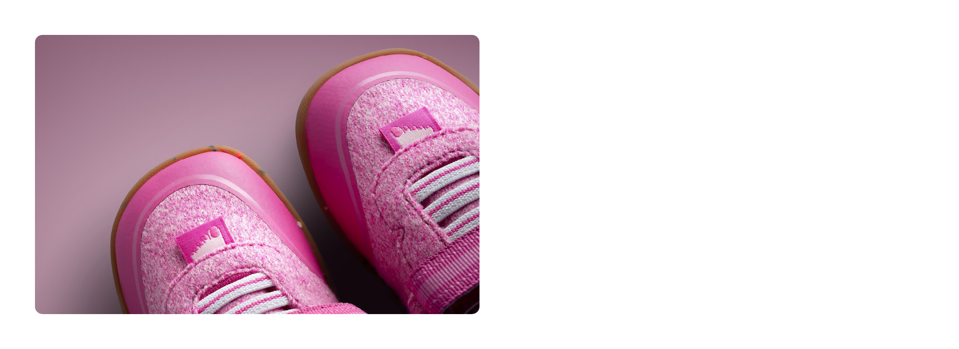 Nahaufnahme zweier pinker Giesswein Kinderschuhe mit Merino-Obermaterial, elastischen Schnürsenkeln und honigfarbener Sohle vor rosa Hintergrund.