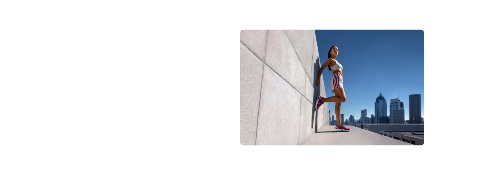 Frau in weißem Sport-BH und gestreiften Shorts mit roten Sneakers beim Laufen auf städtischer Dachterrasse mit Wolkenkratzern und blauem Himmel im Hintergrund.