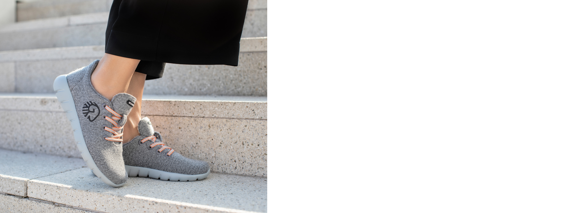 Die Füße einer Person stehen auf einer Treppenstufe. Sie trägt graue Sneakers (Merino Runners von Giesswein) mit weißen Sohlen und orangen Schnürsenkeln. Auf den Schuhen ist das Giesswein-Logo zu sehen. Die Person trägt eine schwarze Hose, und im Hintergrund sind die Stufen der Treppe sichtbar.