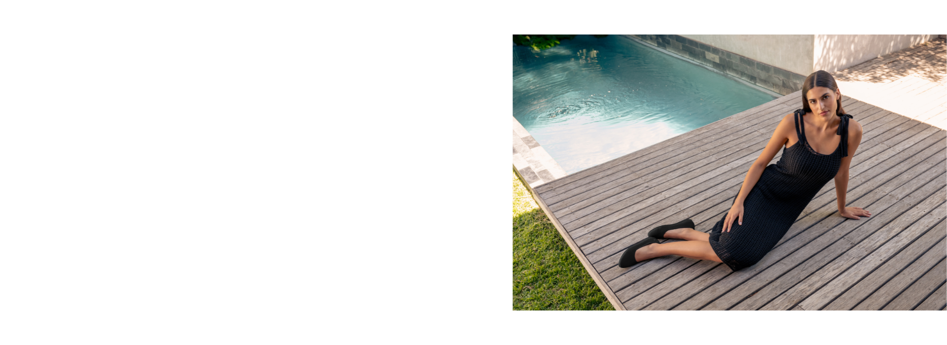 Eine Frau sitzt entspannt auf einer Holzterrasse neben einem Pool. Sie trägt ein schwarzes, ärmelloses Sommerkleid mit Schleifen an den Schultern sowie schwarze Ballerinas (Eco Ballerinas von Giesswein). 